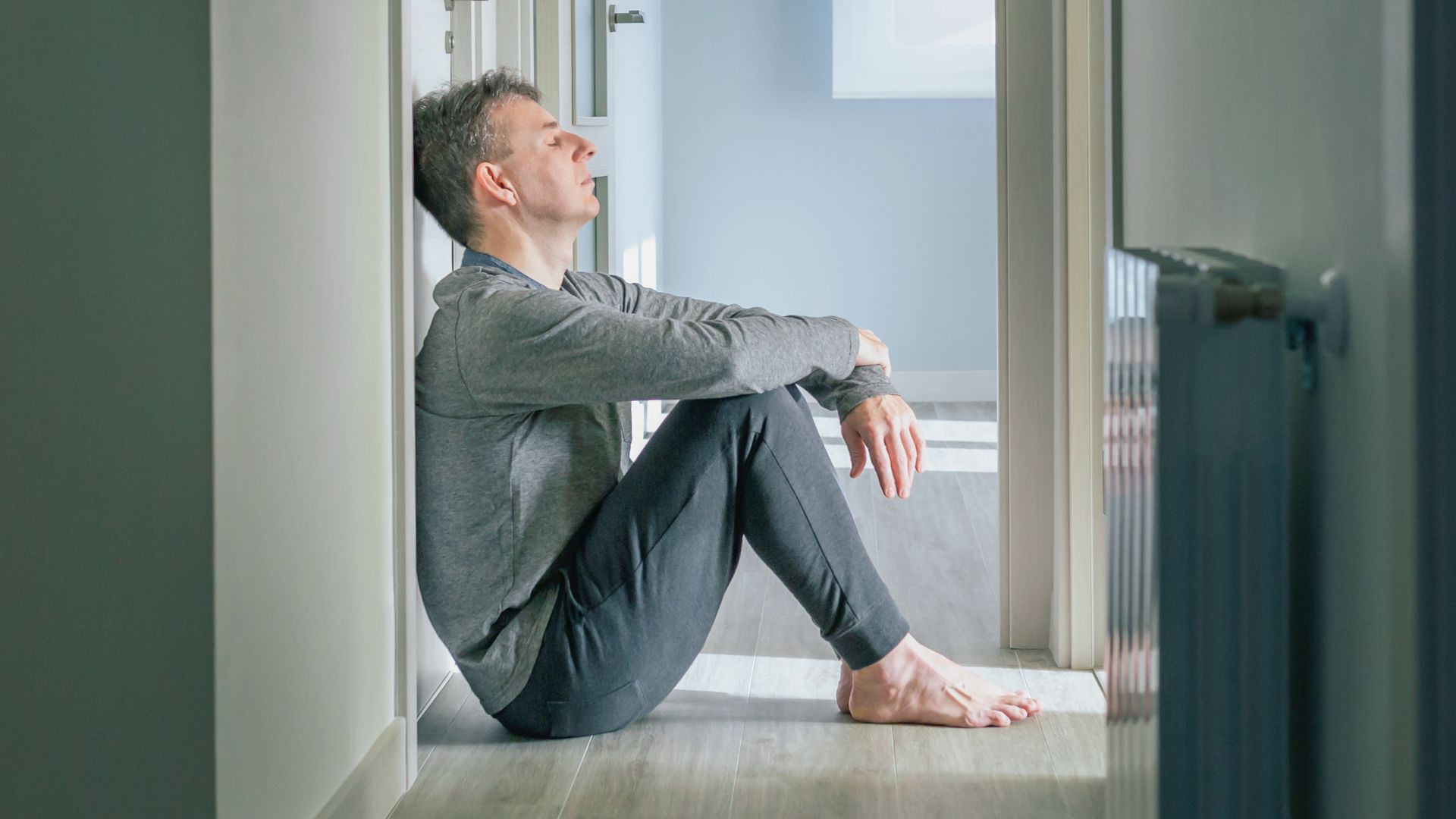 Man sitting in hallway of empty apartment with head leaning against the wall